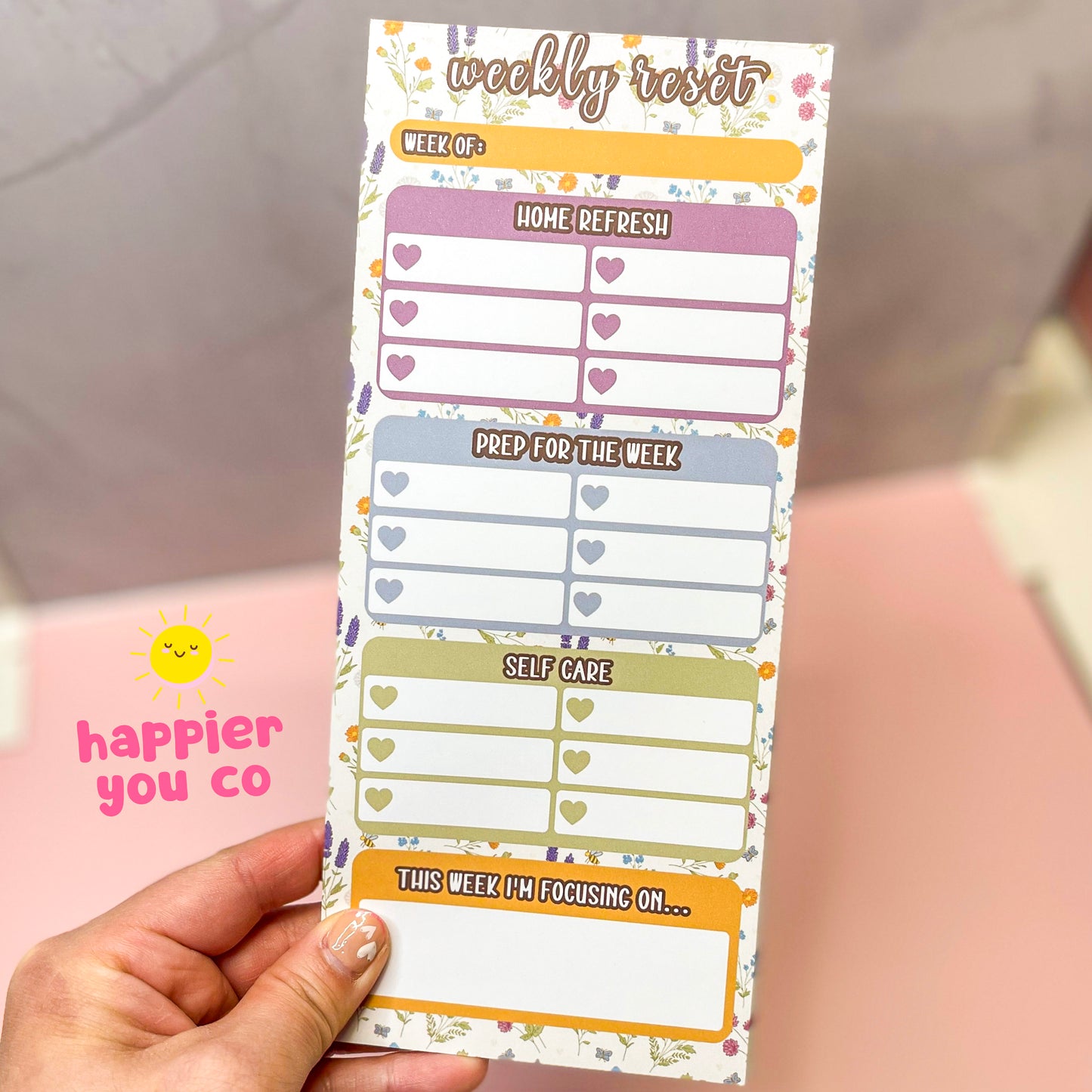 Weekly reset planner pad with a wildflower background held by a hand with a blurred background.