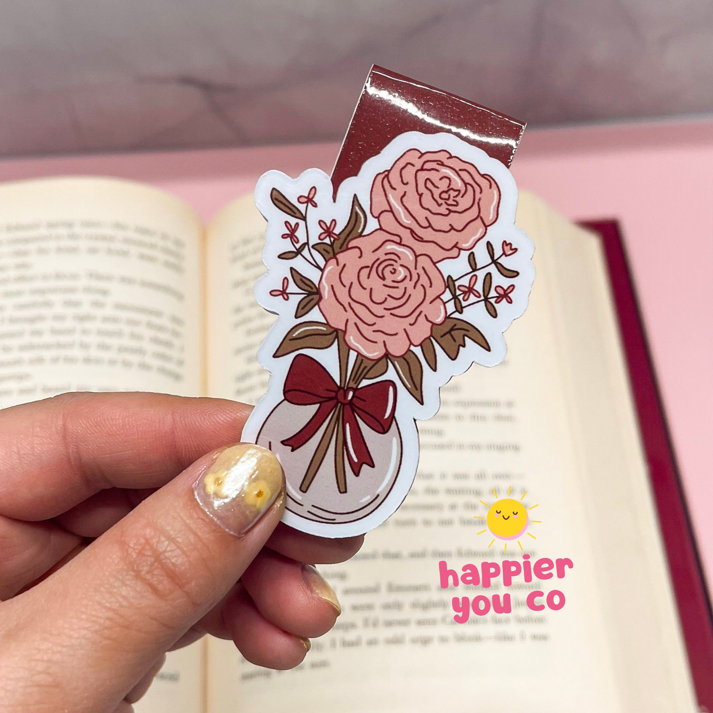 Floral design bookmark held by a hand with an open book in the background