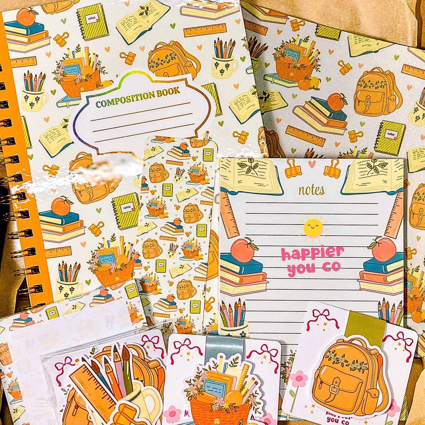 A flat lay of school-themed stationery and a composition book featuring a repeating illustration pattern of backpacks, books, notebooks, pencils, and apples on a white background. The composition includes multiple matching paper items and sticker cards.
