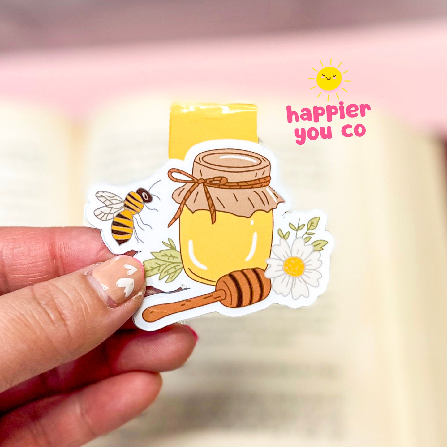 Honey-themed sticker held by a hand with 'happier you co' branding in the background.