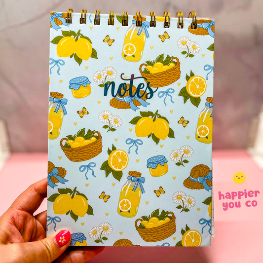 Notebook with lemon-themed design held by a hand, featuring the brand 'happier you co'.