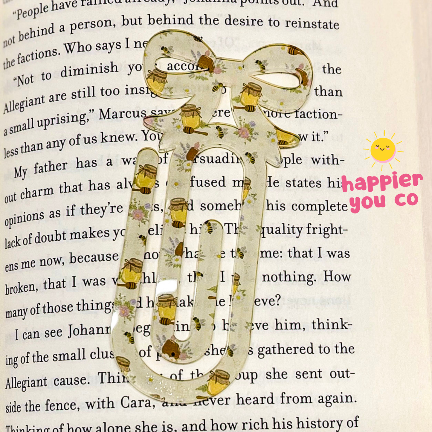 Decorative paperclip with floral design on a book page, featuring 'happier you co' branding.