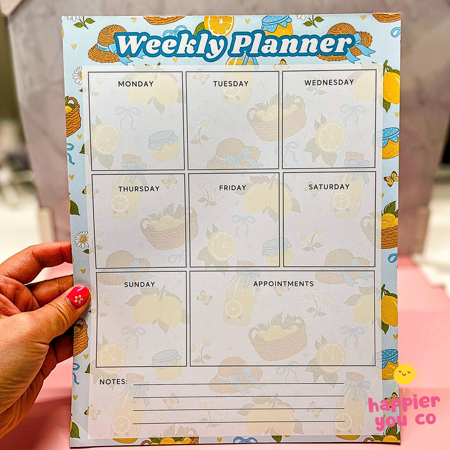 Weekly planner with lemon and daisy design held by a hand