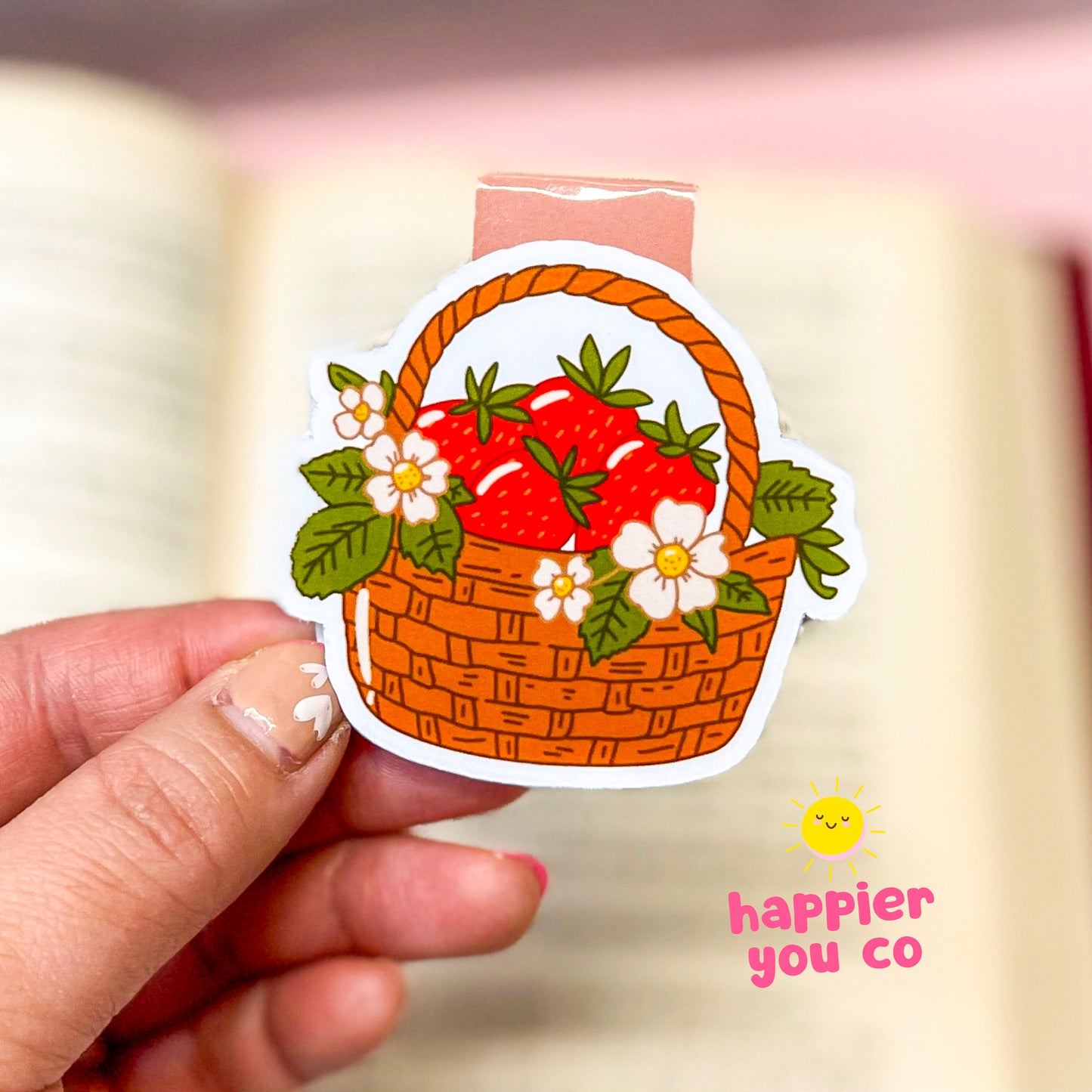 Magnetic bookmark of a basket with strawberries held by a hand, with 'happier you co' branding.