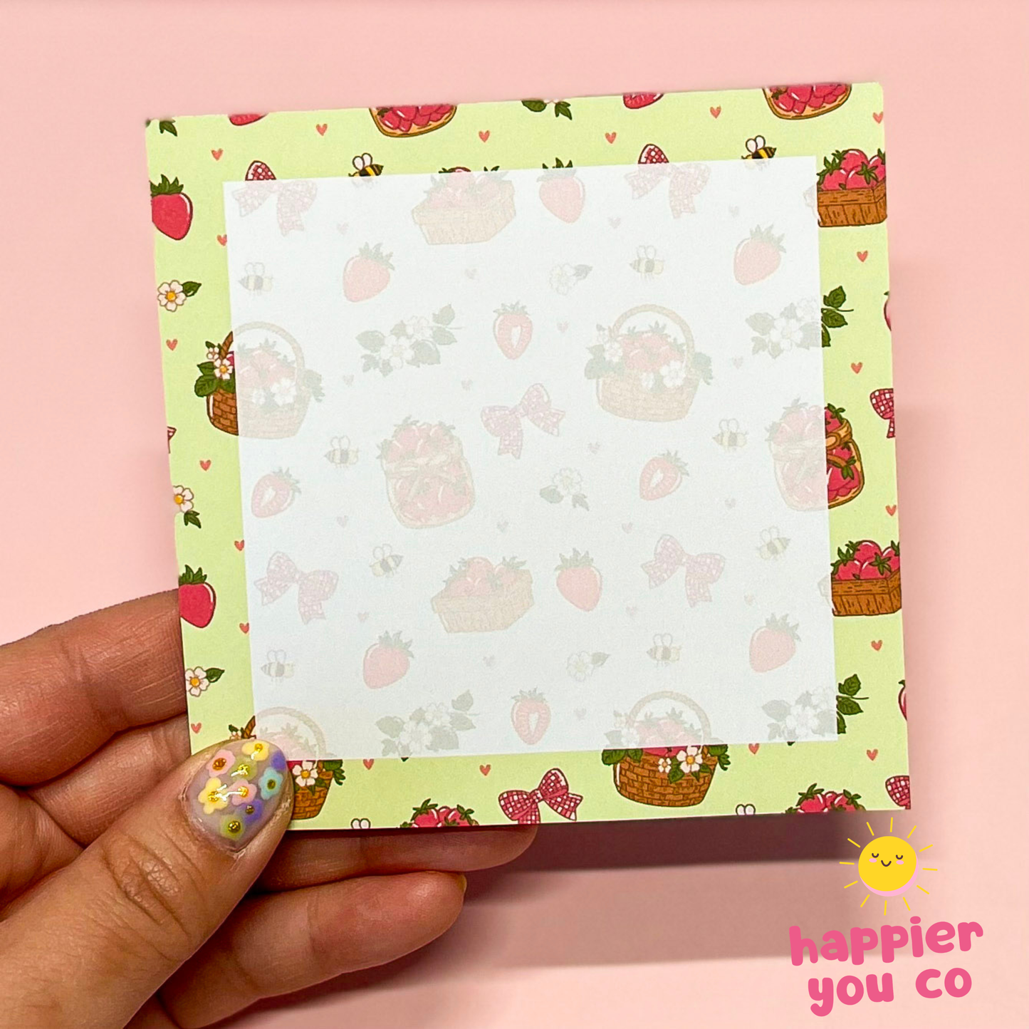 Hand holding a small notepad with a colorful strawberry pattern on a pink background