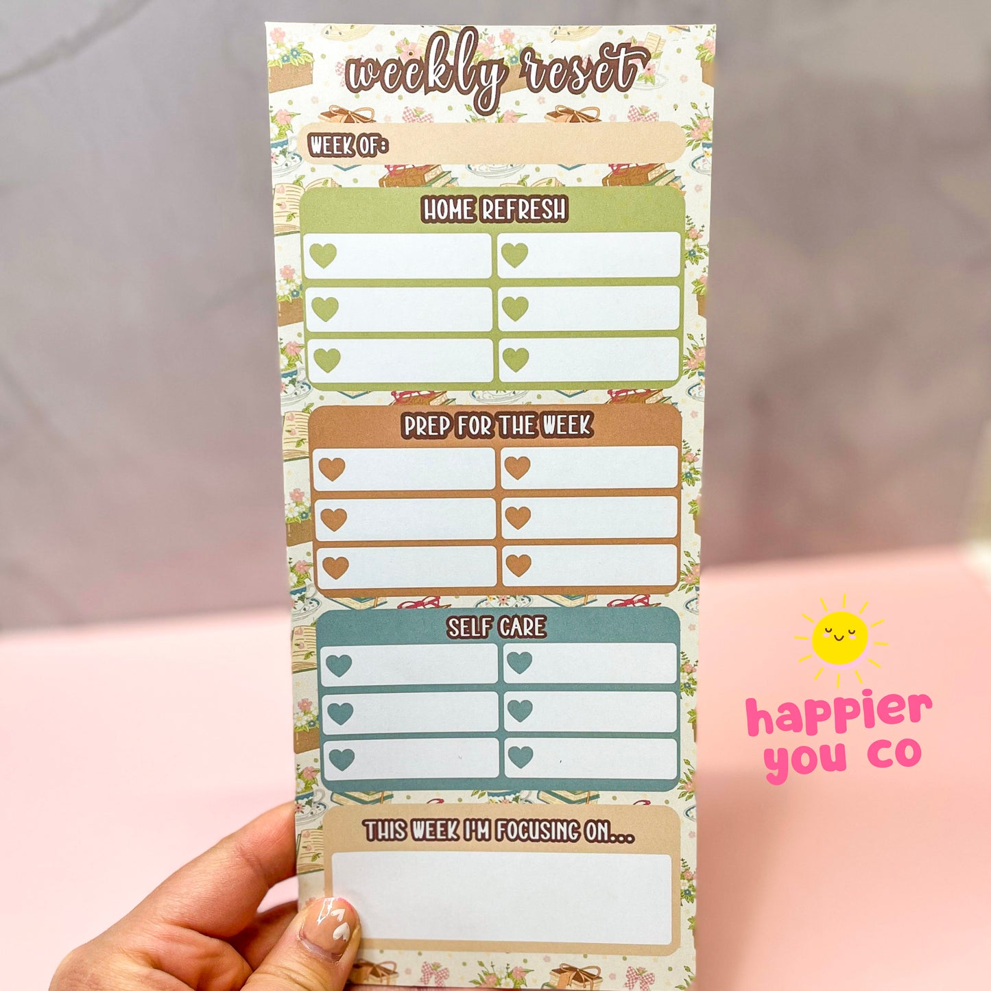 Weekly reset planner sticky notes held by a hand with 'happier you co' branding with a book floral background.