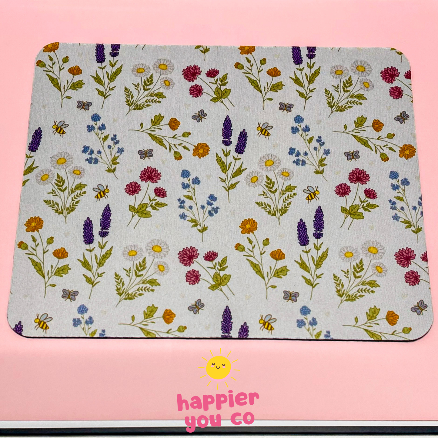 Floral patterned mouse pad with 'happier you co' branding on a pink background