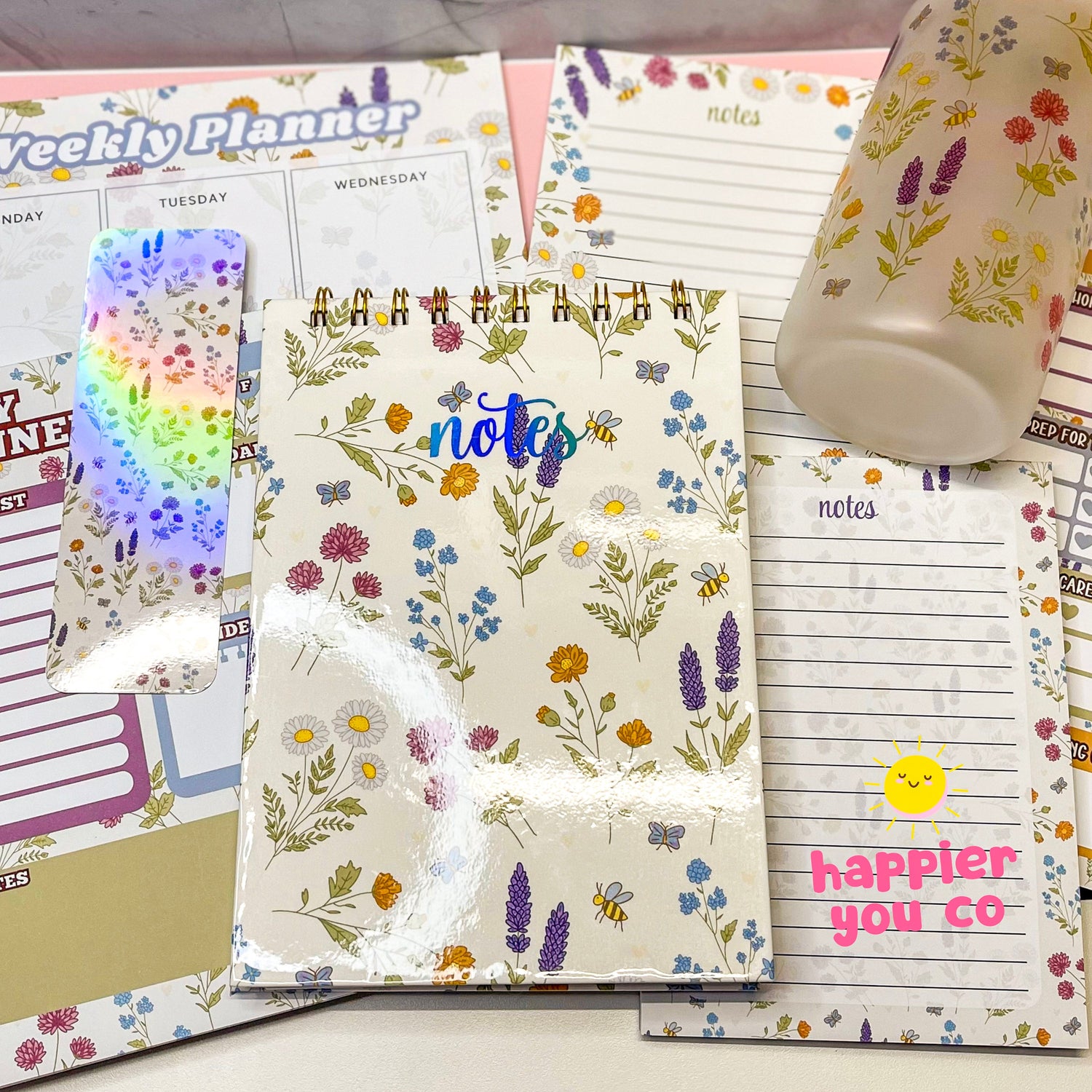 Variety of stationary products that includes notepads, notebooks, planners, bookmarks featuring a floral design