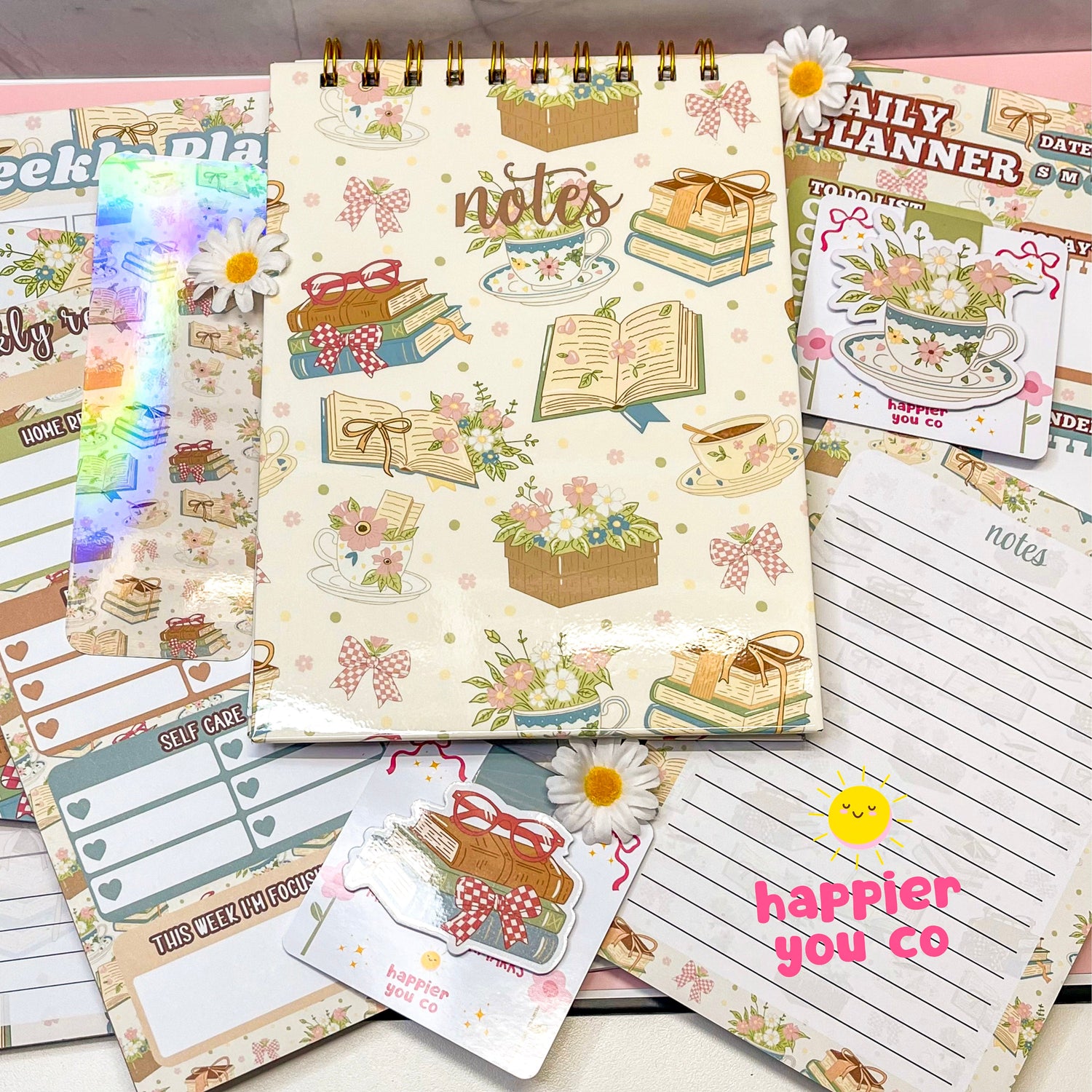 Variety of stationary products that includes notepads, notebooks, planners, bookmarks featuring a floral book design