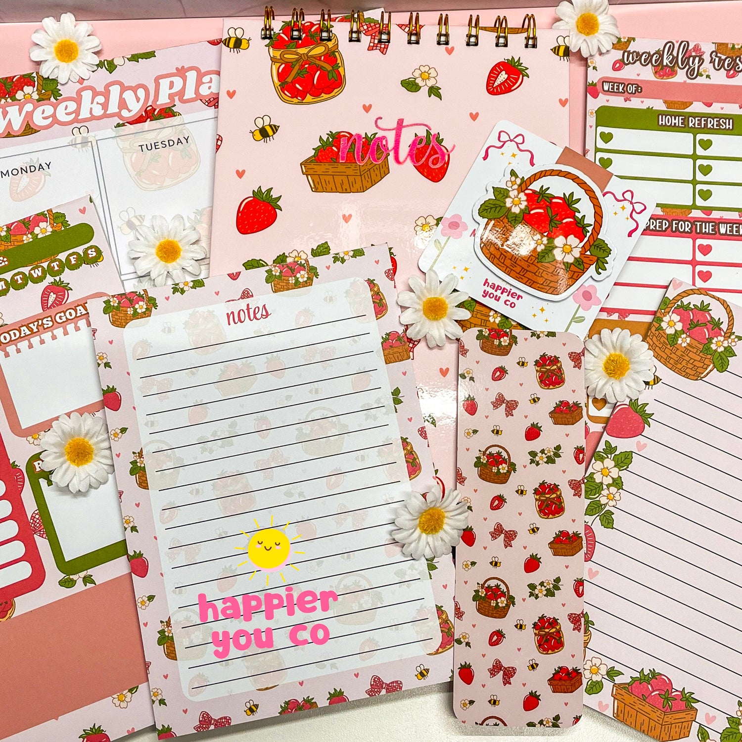 Variety of stationary products that includes notepads, notebooks, planners, bookmarks featuring a strawberry floral design