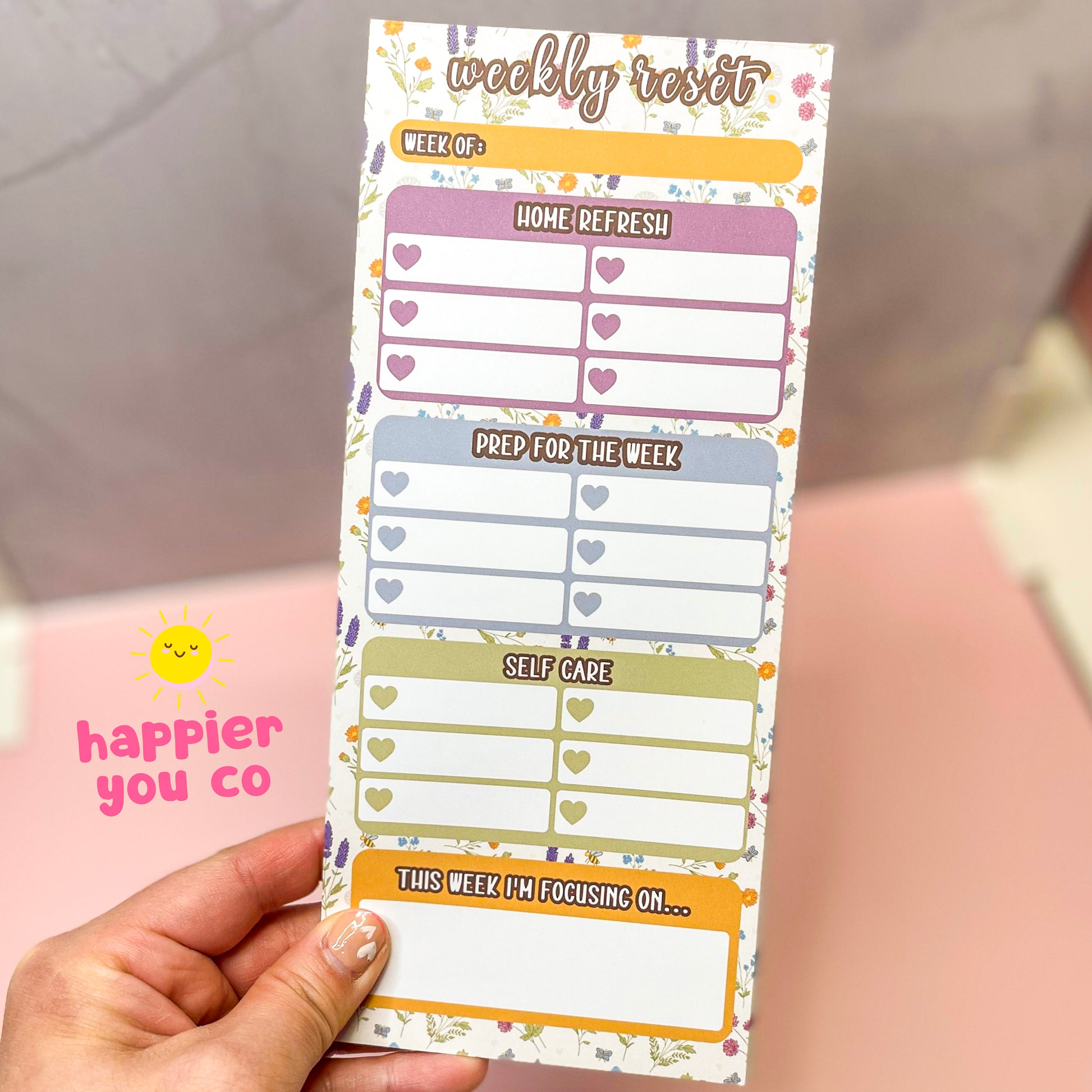 Weekly reset planner pad with a wildflower background held by a hand with a blurred background.