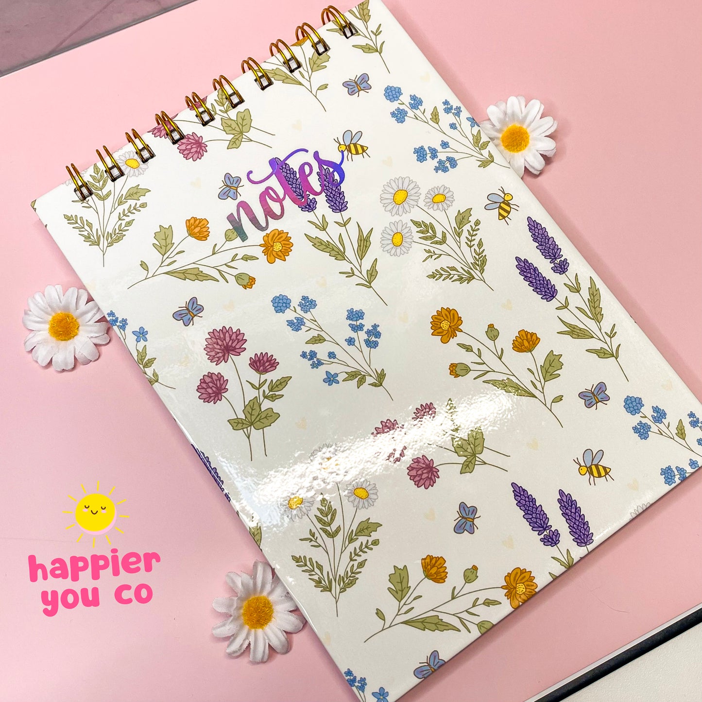 Notebook with floral pattern on a pink background, featuring the brand 'Happier You Co'.