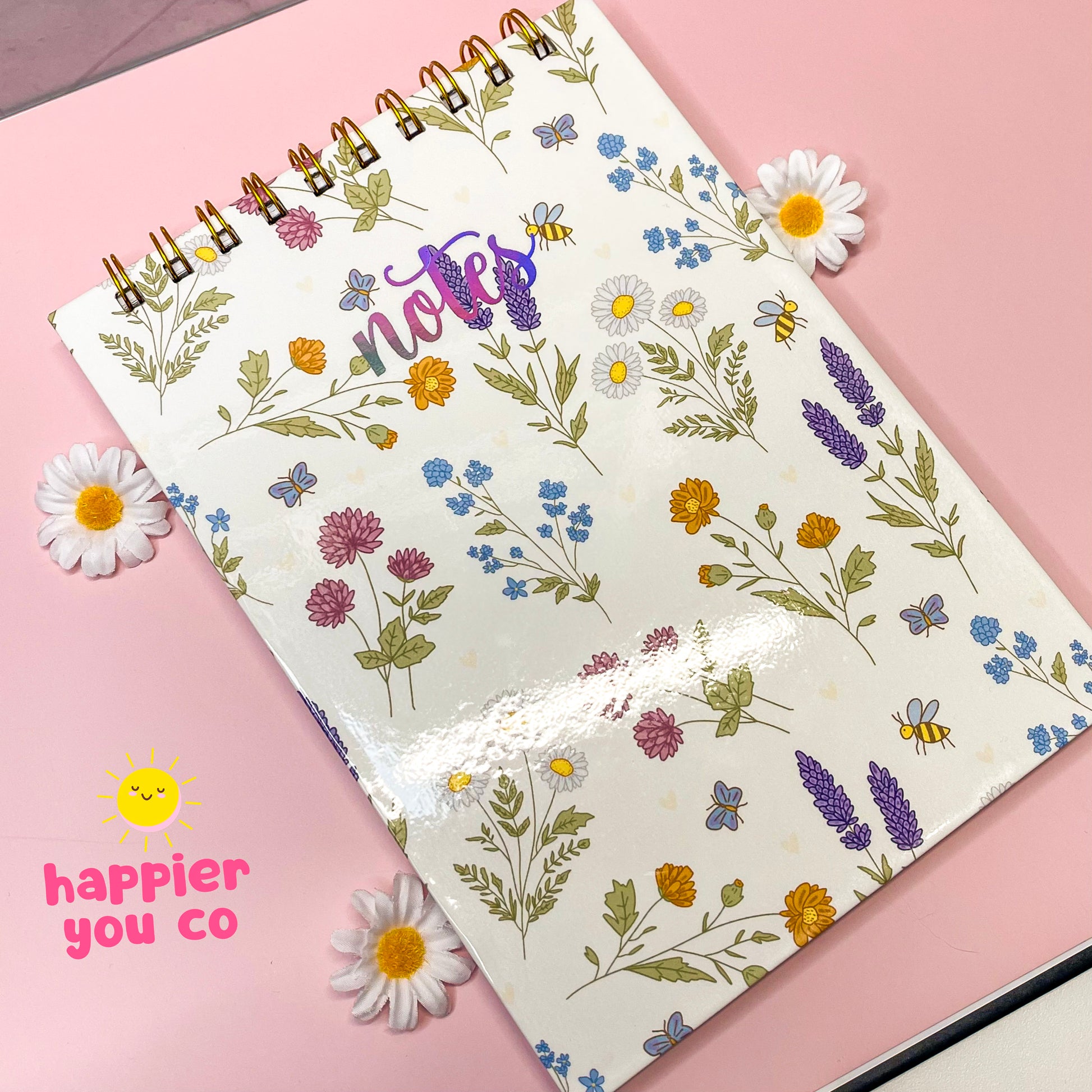 Notebook with floral pattern on a pink background, featuring the brand 'Happier You Co'.