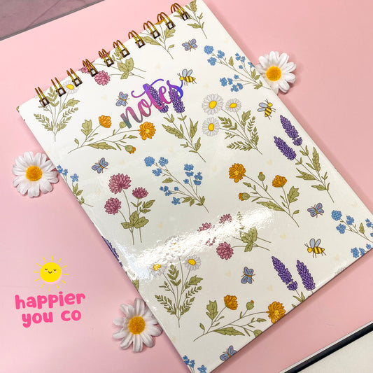 Notebook with floral pattern on a pink background, featuring the brand 'Happier You Co'.