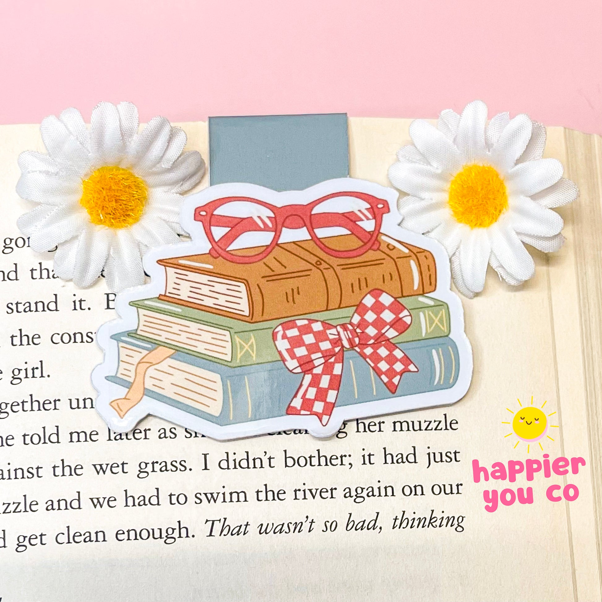 Illustration of books with a bow and sunglasses on a page with flowers, featuring 'happier you co' branding.
