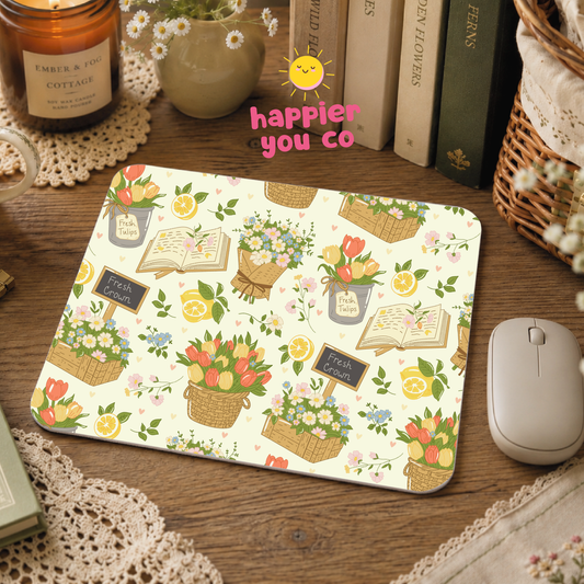 Mouse pad with floral and book design on a wooden desk, featuring 'happier you co' text.