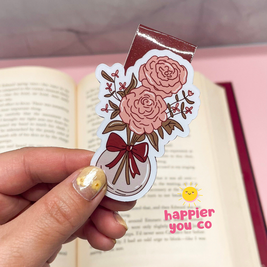 Floral design bookmark held by a hand with an open book in the background