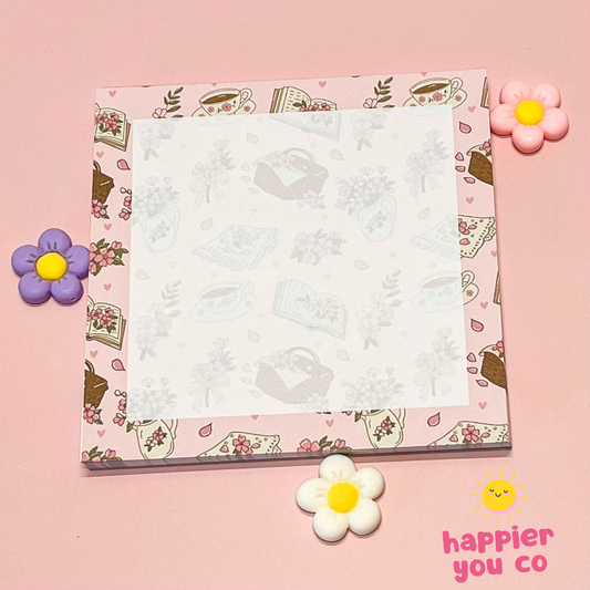 Notepad with floral and tea cup design on a pink background with decorative flowers and 'happier you co' text.