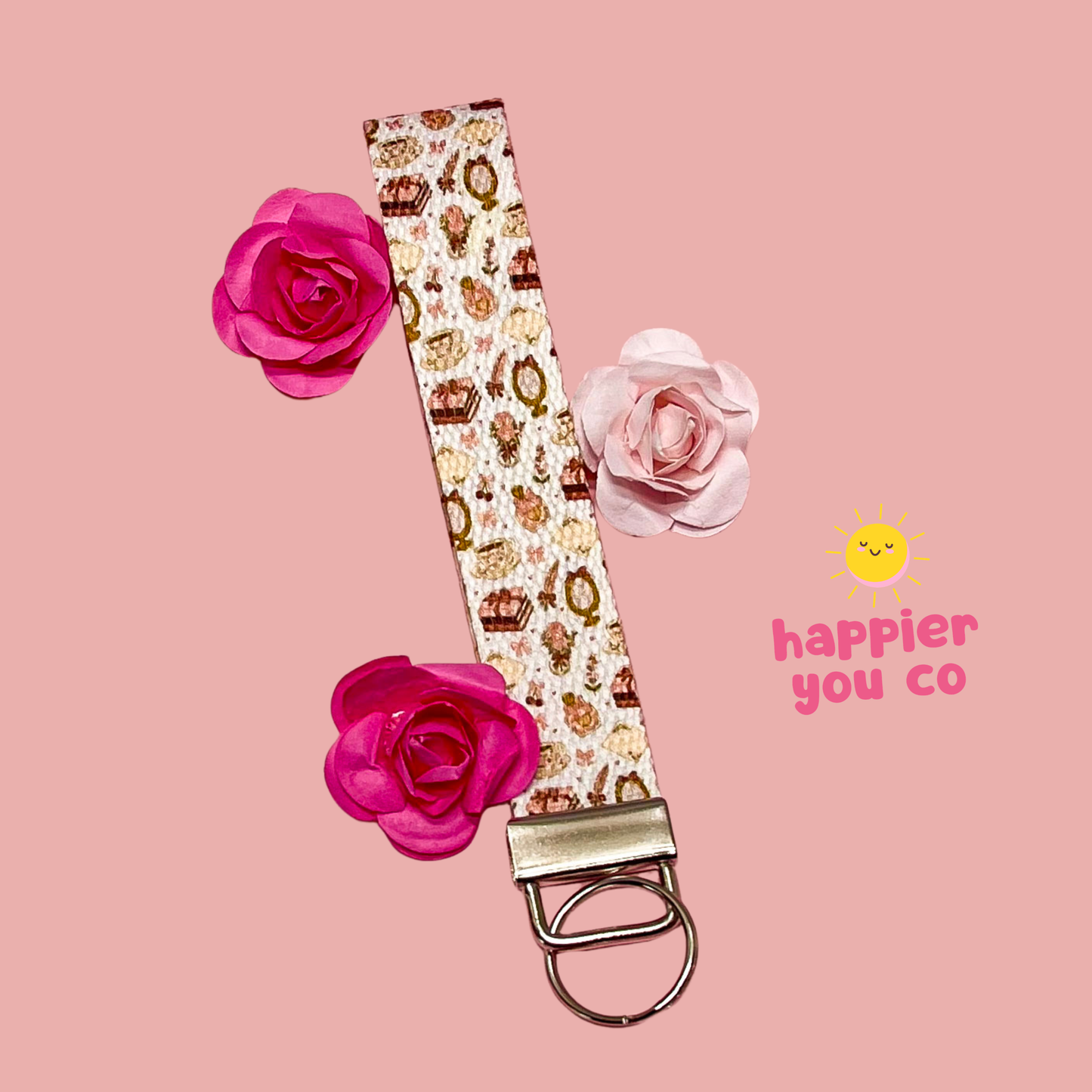 Keychain with floral design and 'happier you co' branding on a pink background