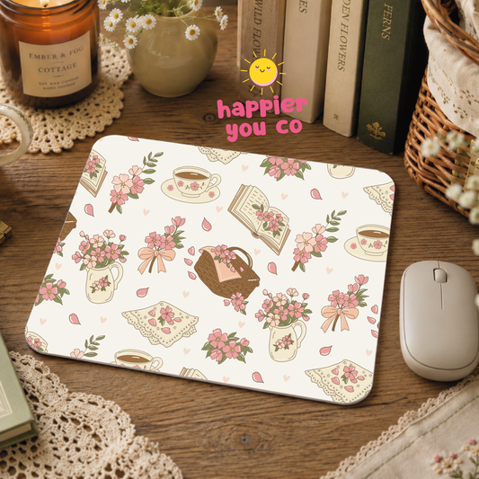 Floral and tea cup patterned mouse pad on a wooden surface with books and a candle.