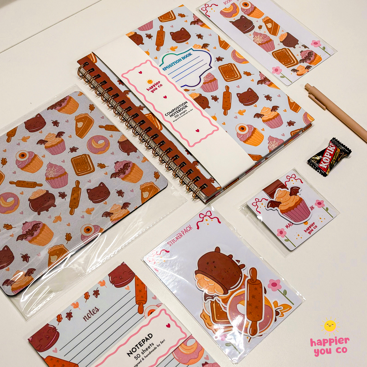 A coordinated stationery set with a spiral-bound notebook, notepad, memo cards, sticker sheets, and a pen, all printed with a warm autumn bakery theme including cupcakes, pastries, cookies, and cinnamon sticks on a white background.