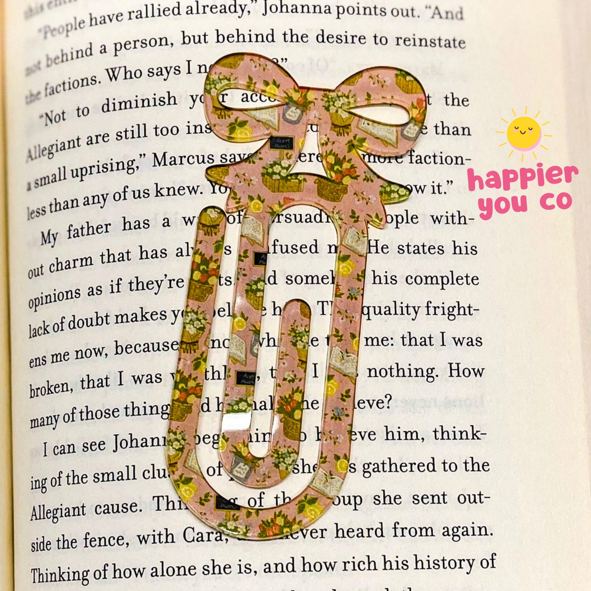 Decorative paper clip with floral pattern on a book page, featuring 'happier you co' text.