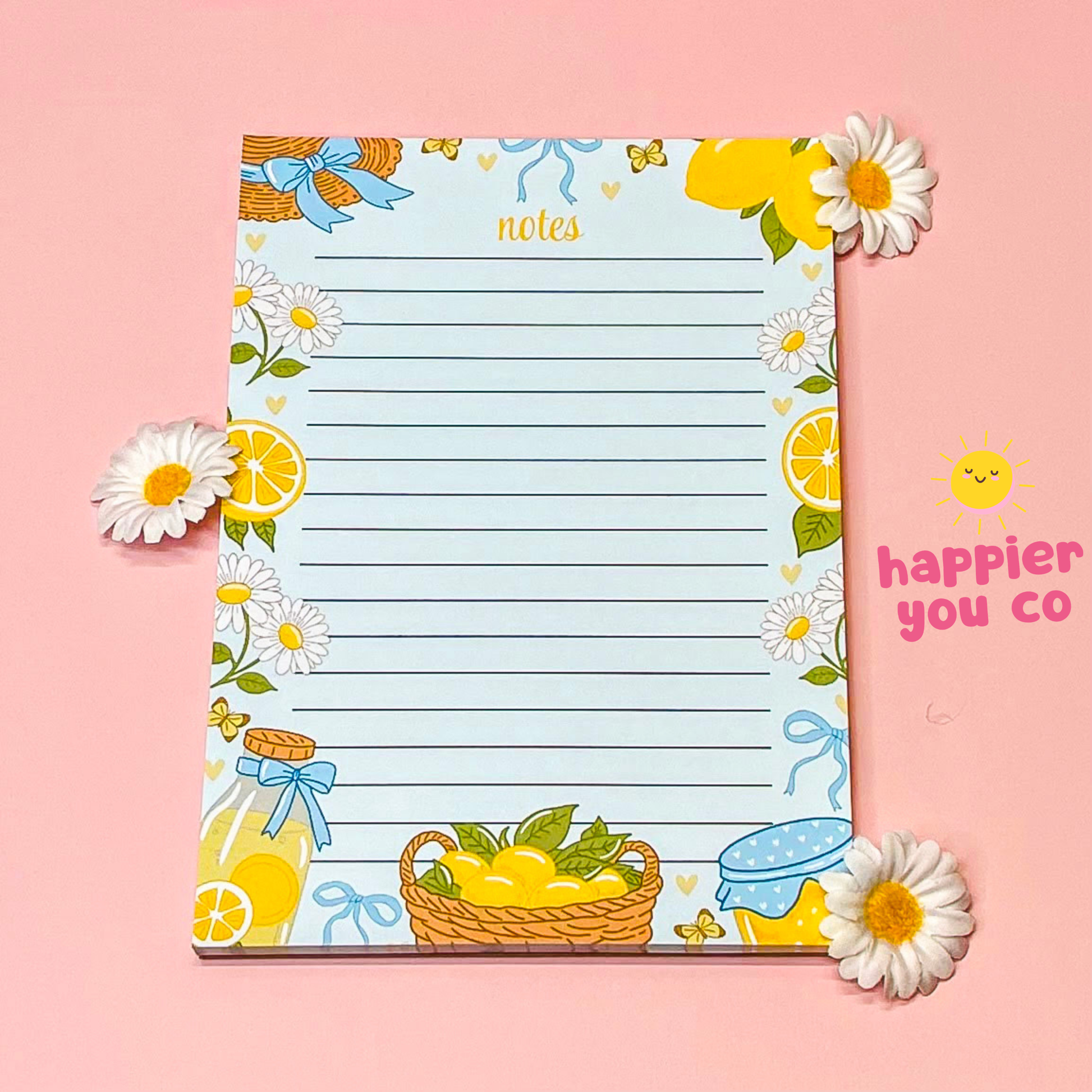 Notepad with lemon and flower design on a pink background, featuring the brand 'happier you co'.