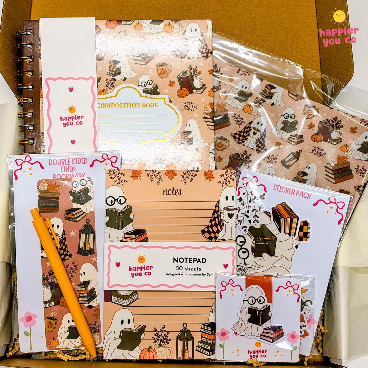 A boxed stationery set with autumn ghost illustrations, including a composition book, notepad, sticker pack, double-sided lined paper, and a pen, arranged in a cardboard box.