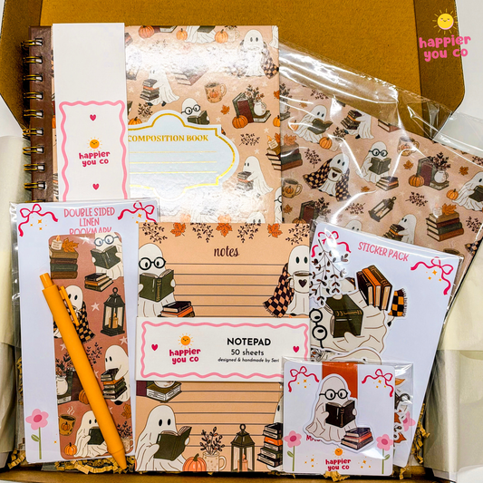 A boxed stationery set with autumn ghost illustrations, including a composition book, notepad, sticker pack, double-sided lined paper, and a pen, arranged in a cardboard box.