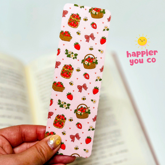Decorative bookmark with strawberry pattern held by a hand, against a light blue background with 'happier you co' branding.