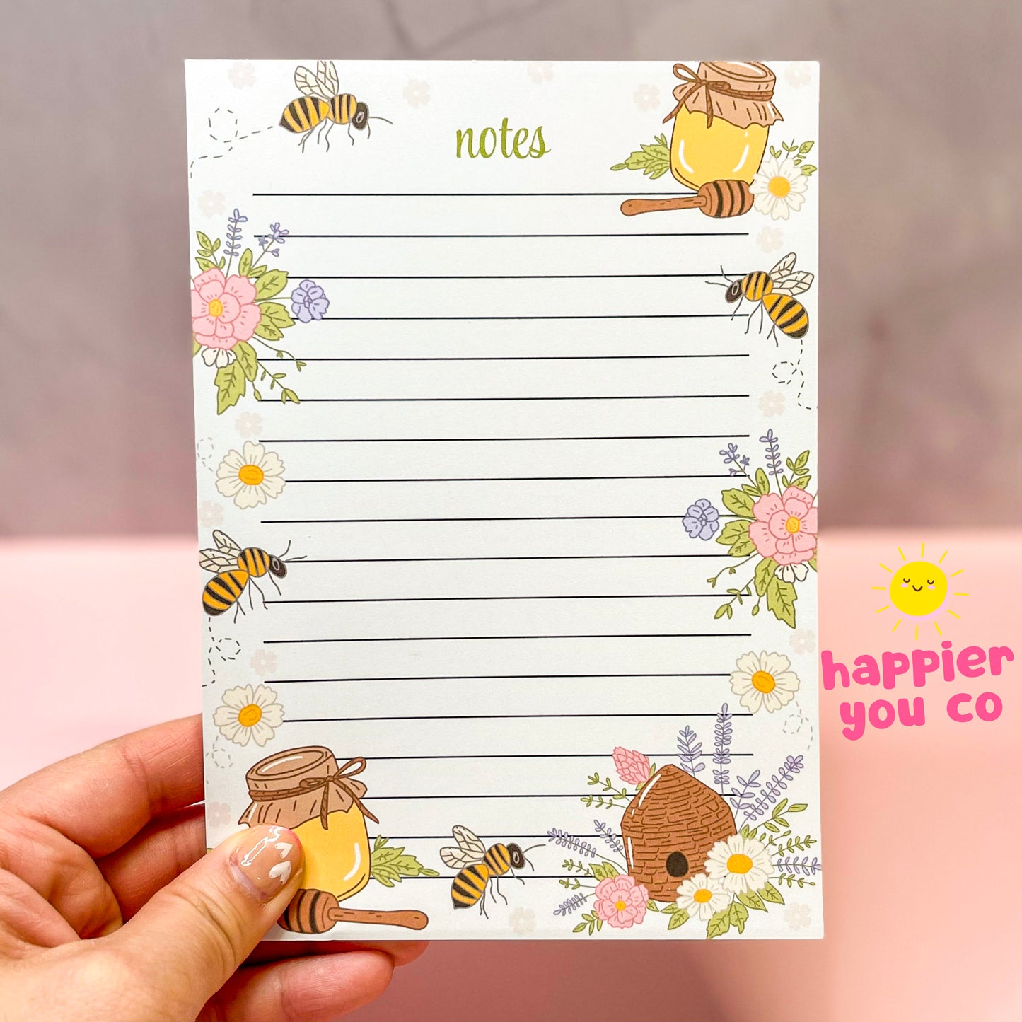 Notebook with bee and honey design held by a hand, brand 'happier you co' visible