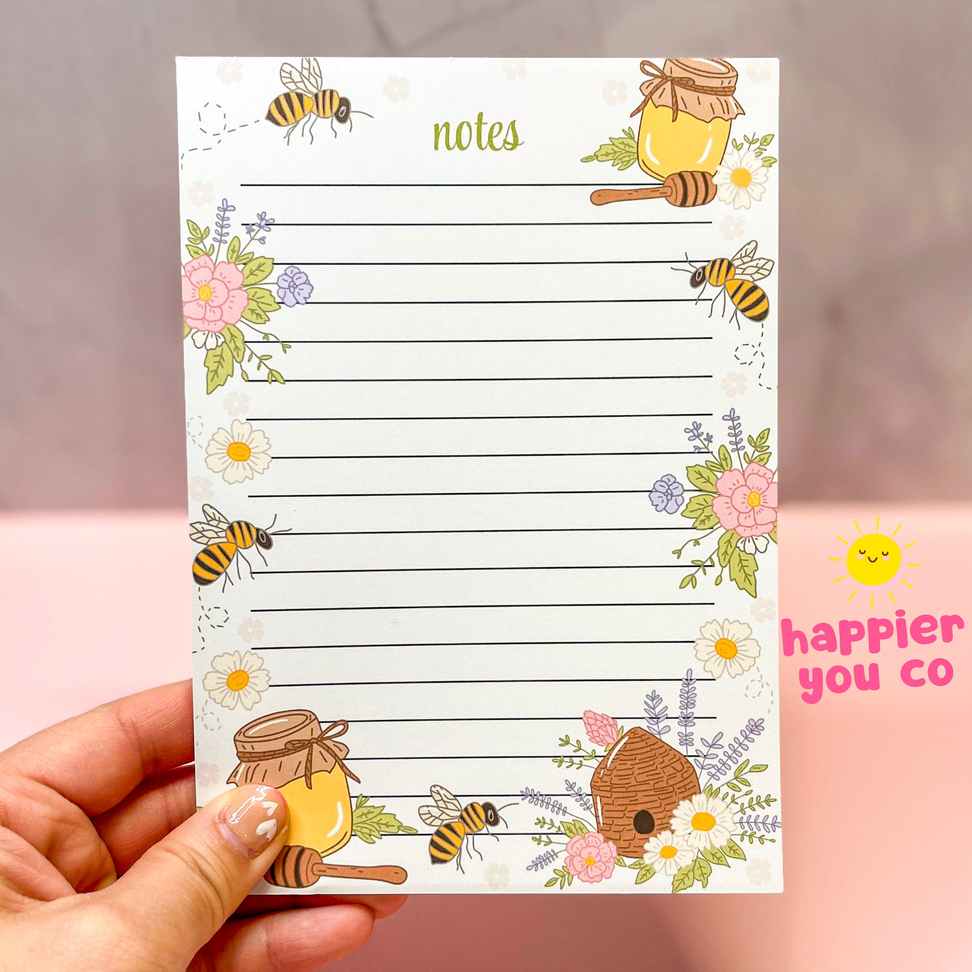 Notebook with bee and honey design held by a hand, brand 'happier you co' visible