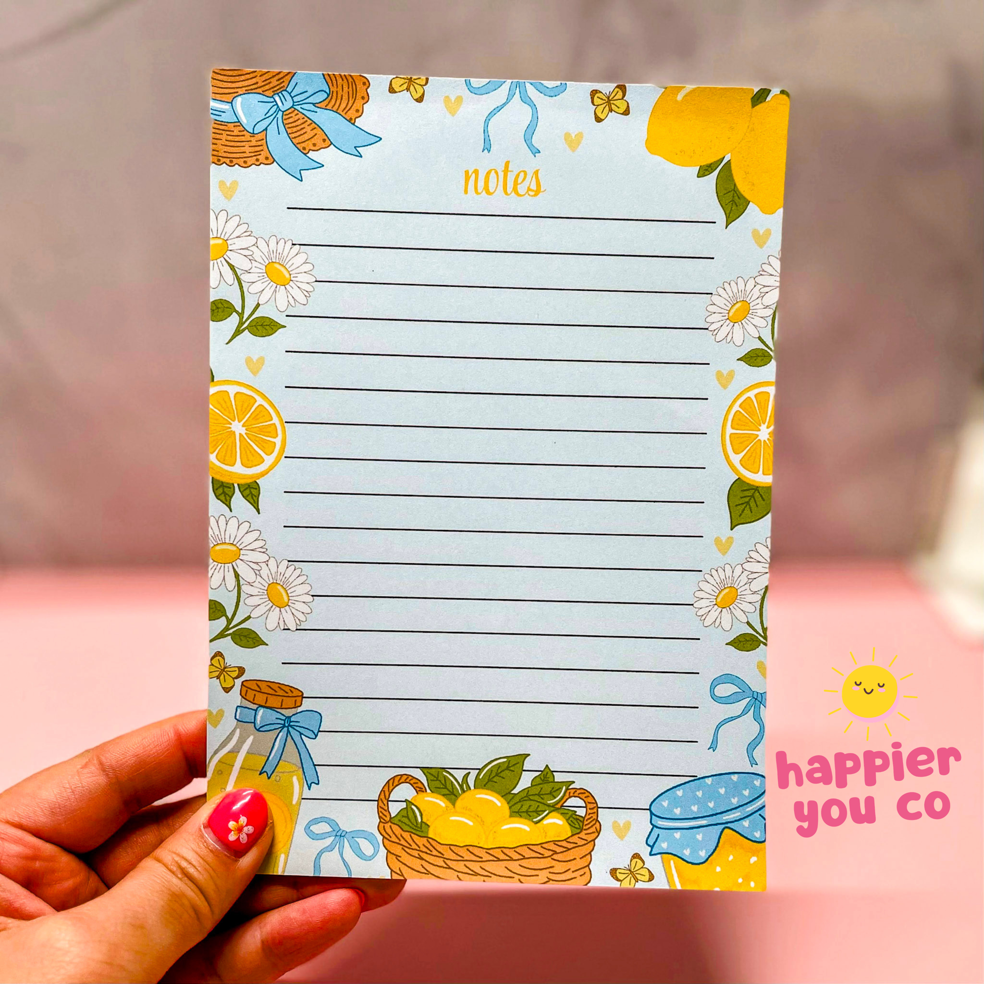 Notepad with floral and lemon design held by a hand, with 'happier you co' branding.