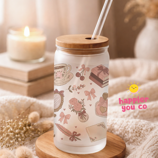Tumbler with wooden lid and straw, featuring illustrations and 'happier you co' branding, on a soft surface with a candle in the background.
