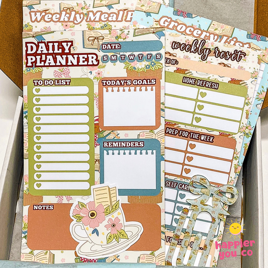 Planner sheets with various sections like 'Weekly Meal', 'Daily Planner', and 'Grocery List' on a wooden surface.