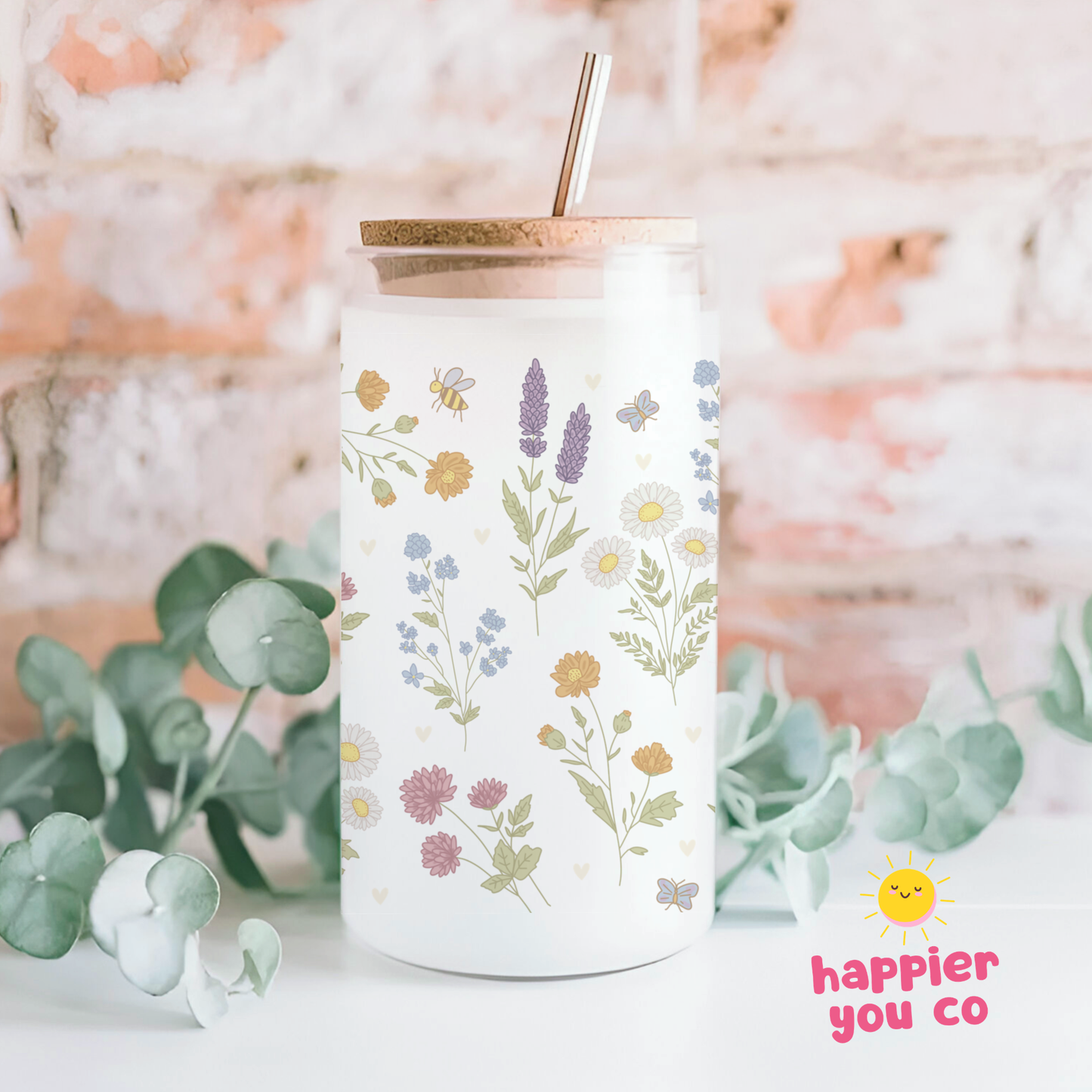 Tumbler with floral design and 'happier you co' branding on a blurred natural background