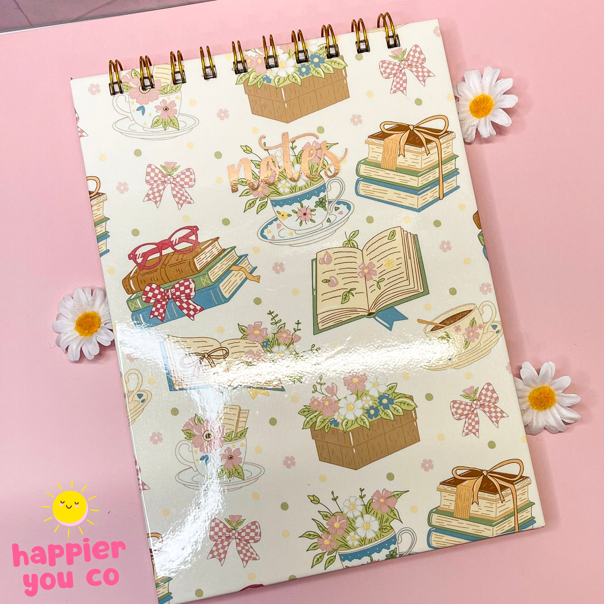 Notebook with decorative cover featuring books, flowers, and boxes on a pink background with daisies.