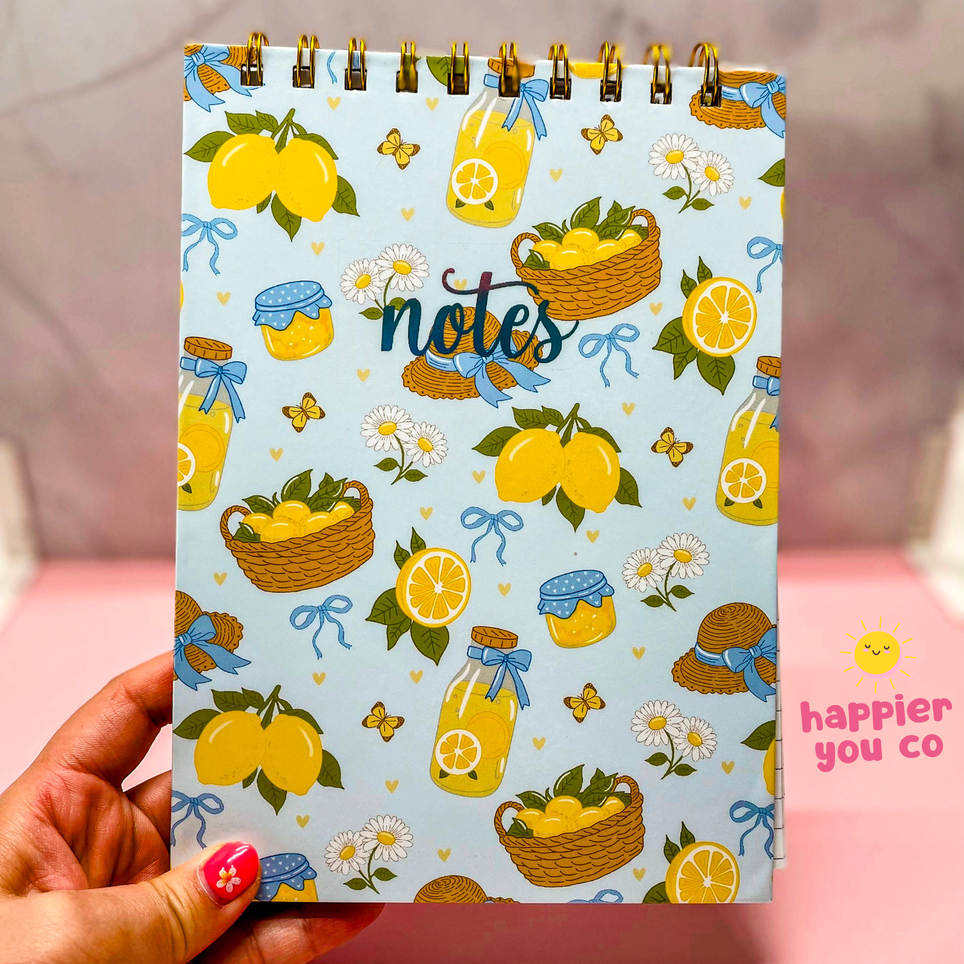 Notebook with lemon-themed design held by a hand, featuring the brand 'happier you co'.