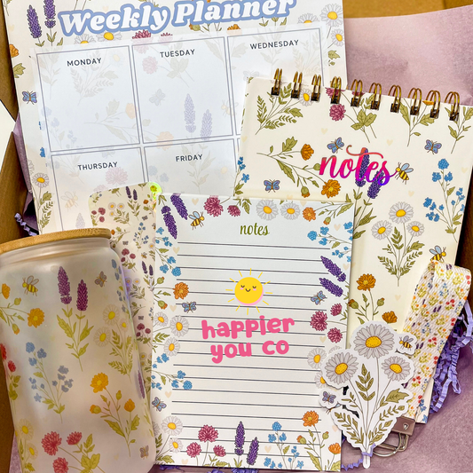 Floral-themed weekly planner and notepad with 'happier you co' on a wooden surface.