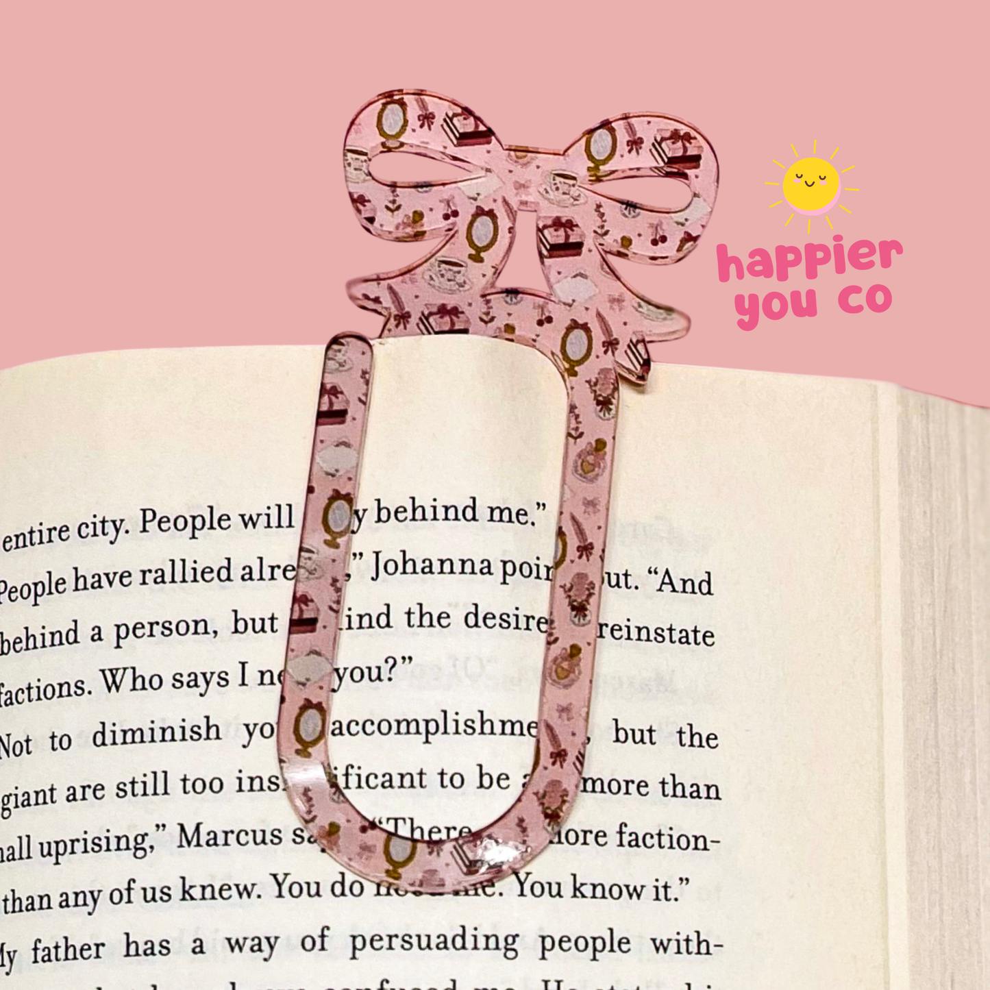 Decorative pink bow-shaped clip on a book with 'happier you co' branding.