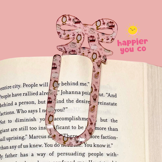 Decorative pink bow-shaped clip on a book with 'happier you co' branding.
