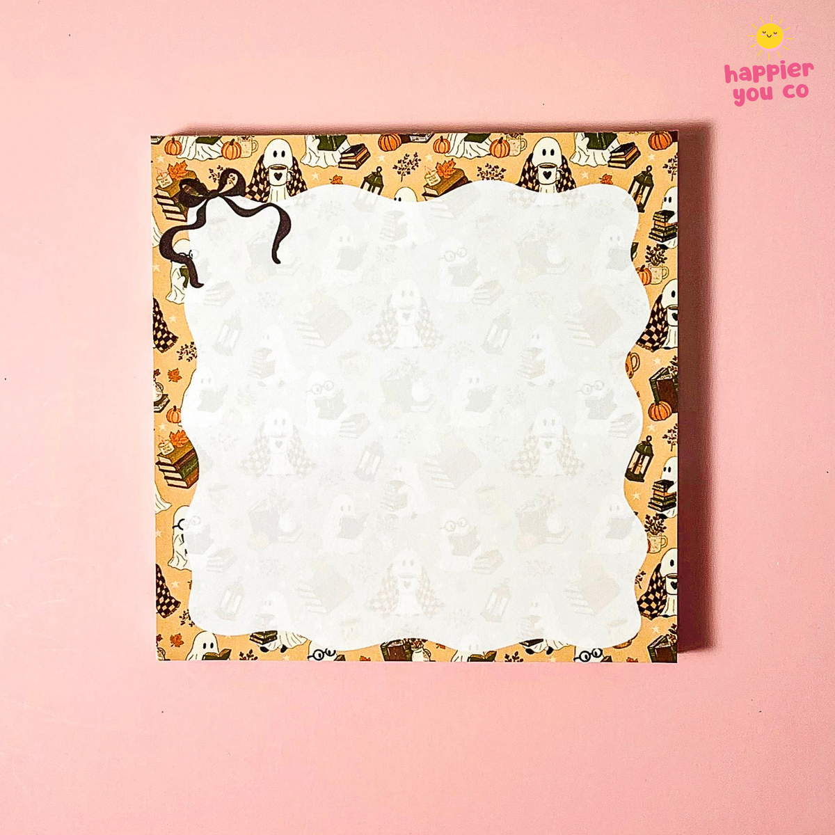 A square notepad with a scalloped white writing area and a Halloween-themed patterned border featuring ghosts, pumpkins, bats, and spiderwebs, shown on a solid pink background.