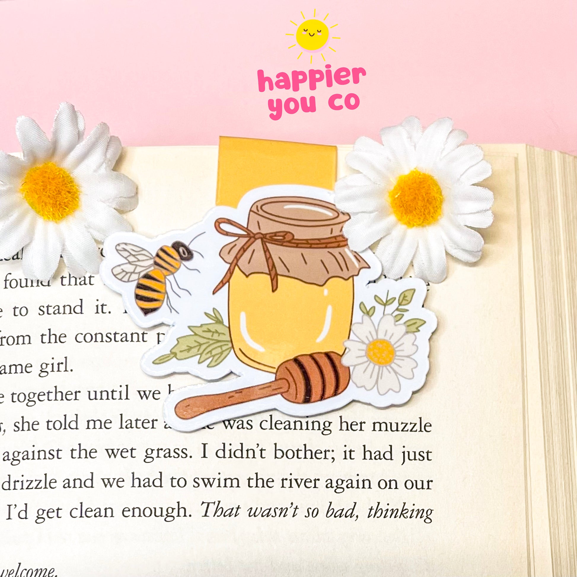 Decorative magnetic bookmark with honey jar, bee, and flowers on a book page with 'happier you' text.