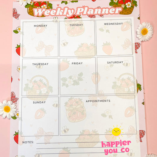 Weekly planner with a strawberry floral background on a pink table 
