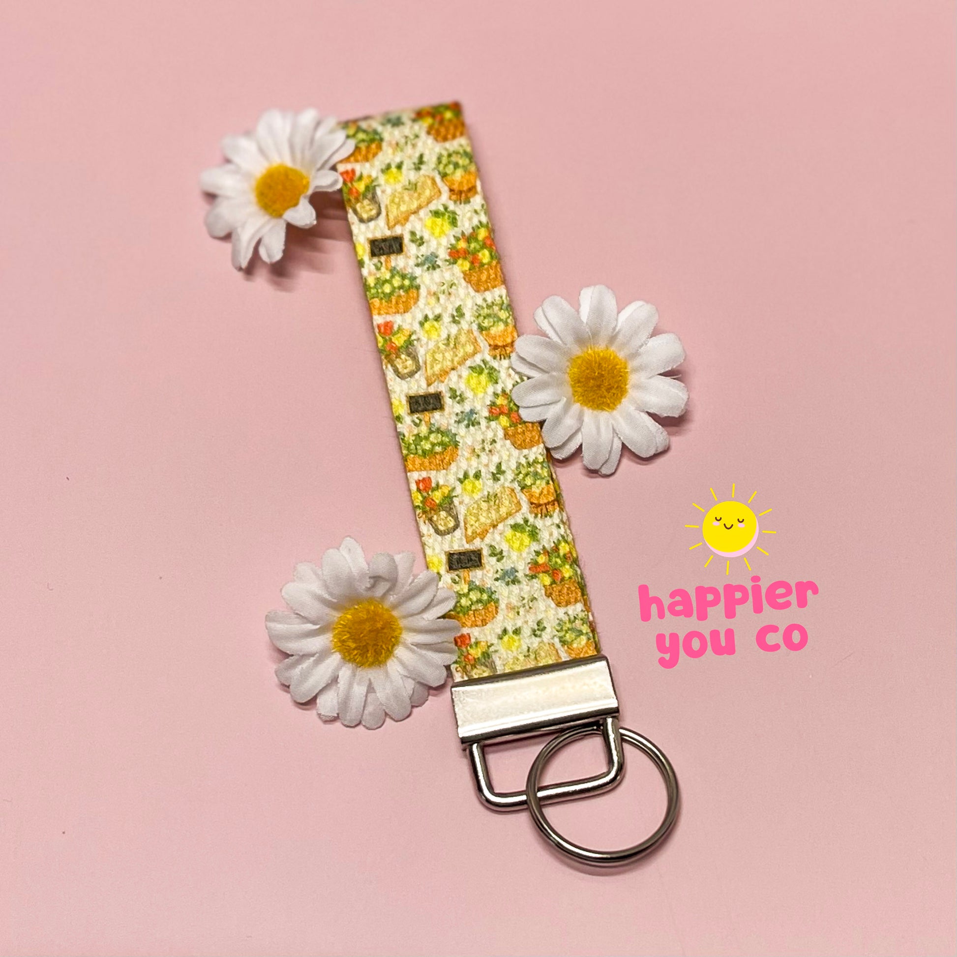Keychain with floral pattern and daisies on a pink background, featuring 'happier you co' branding.