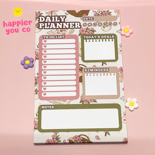 Daily planner with floral design on a pink background, featuring the brand 'happier you co'.