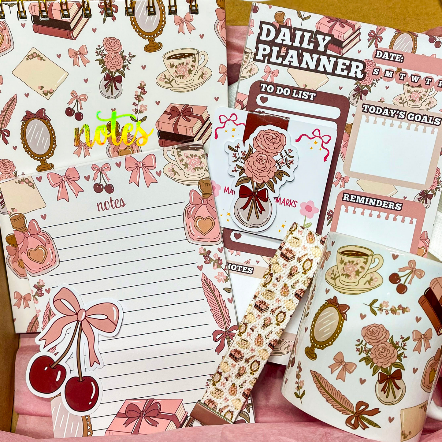 Stationery items including a planner, to-do list, and mug with decorative designs on a pink background.