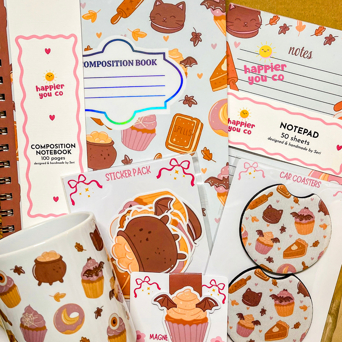 A collection of cute, autumn-themed stationery items featuring a consistent design with cartoon cats, cupcakes, and fall leaves. The set includes a composition notebook, a notepad, a sticker pack, car coasters, and a mug, all decorated with pastel colors and illustrated with playful cat and dessert motifs.