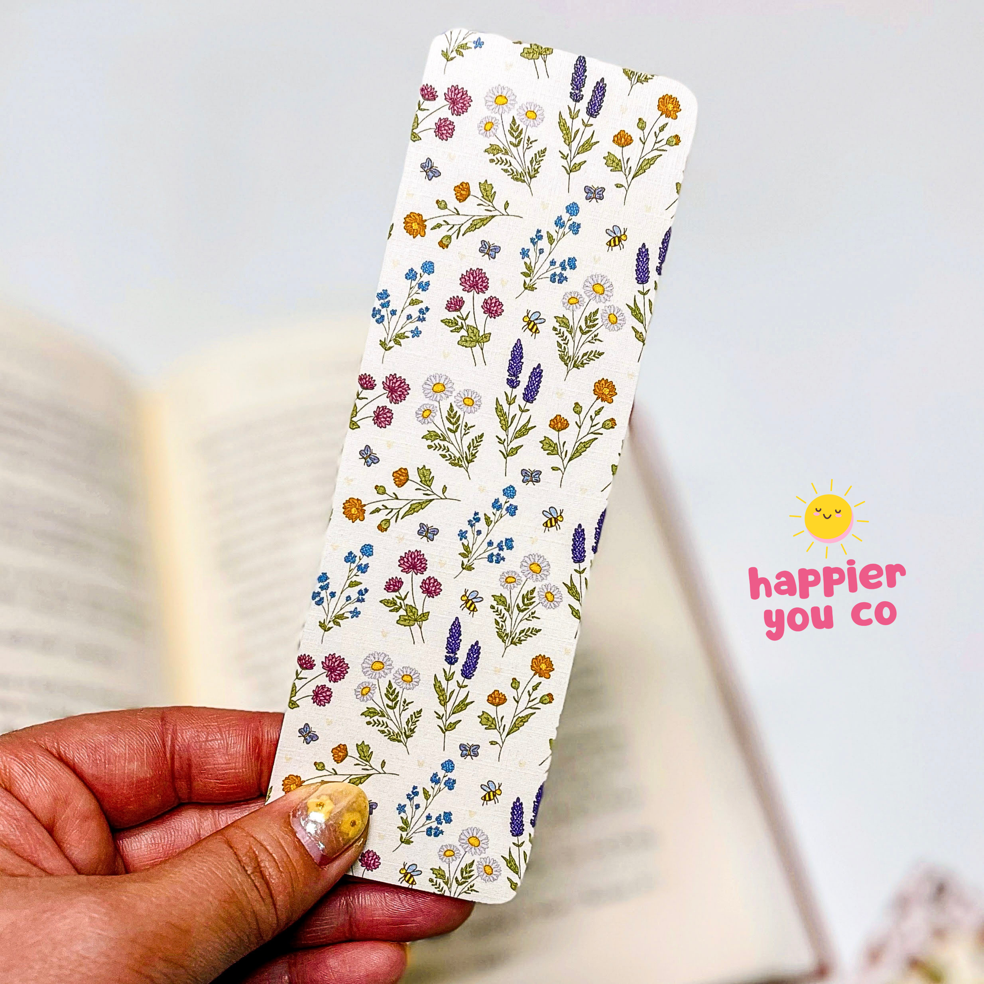 Floral-patterned bookmark held by a hand with 'happier you co' branding.