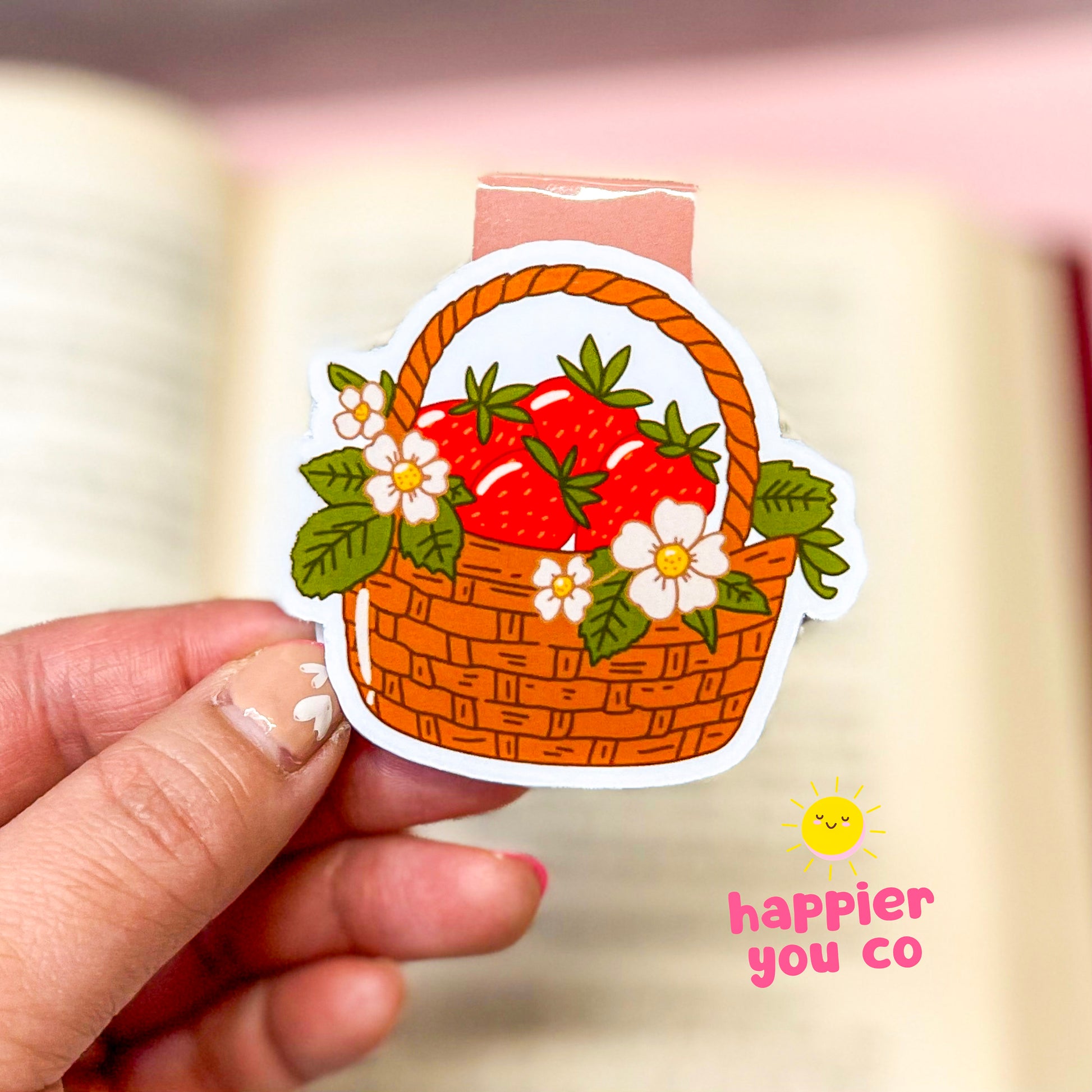 Magnetic bookmark of a basket with strawberries held by a hand, with 'happier you co' branding.